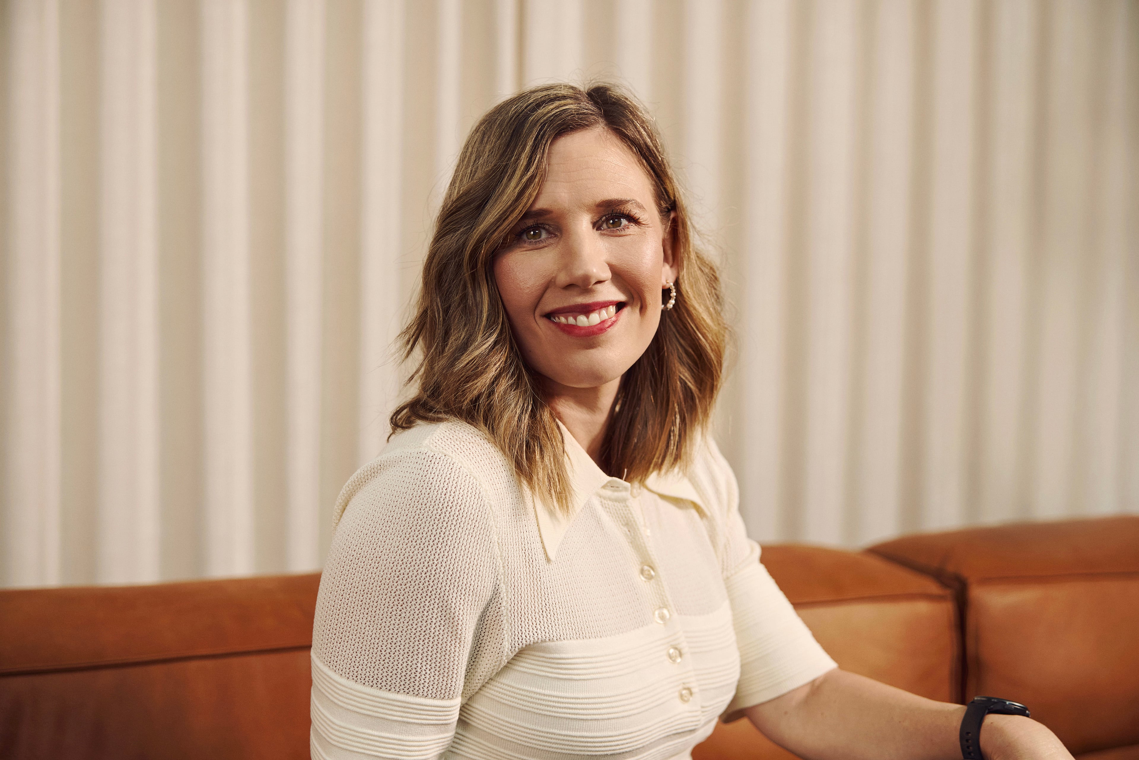 Woman in white blouse sitting on brown sofa in front of light gray curtain