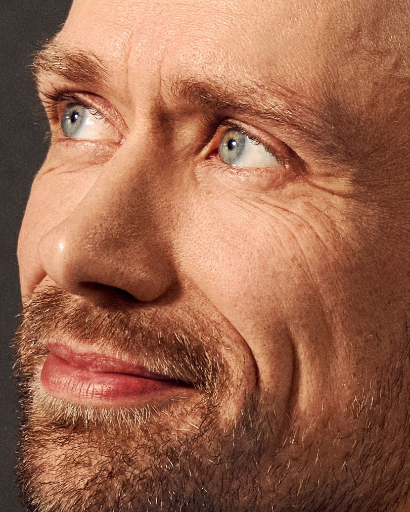 Man with red beard and blue eyes looking directly at camera against dark background