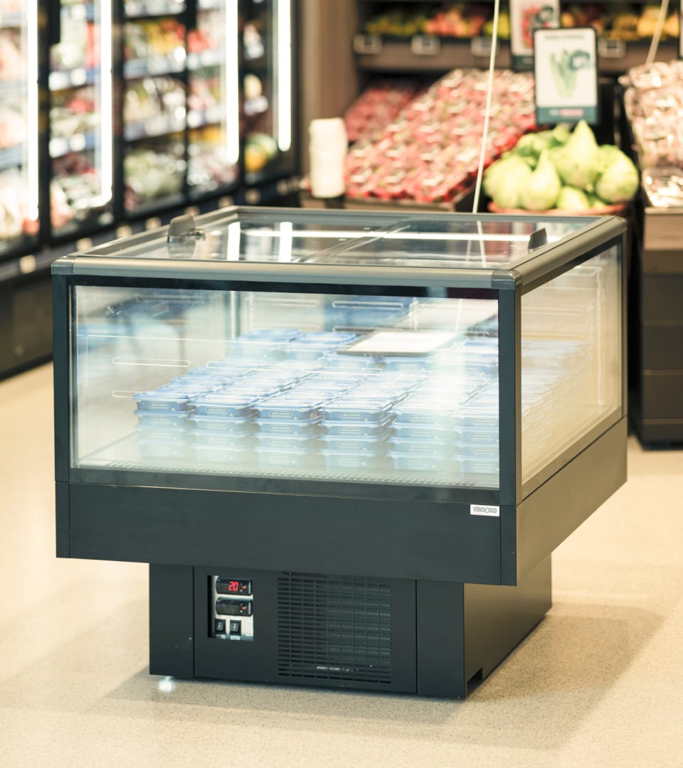 Refrigerated display case with glass doors containing blue packaged products in a grocery store