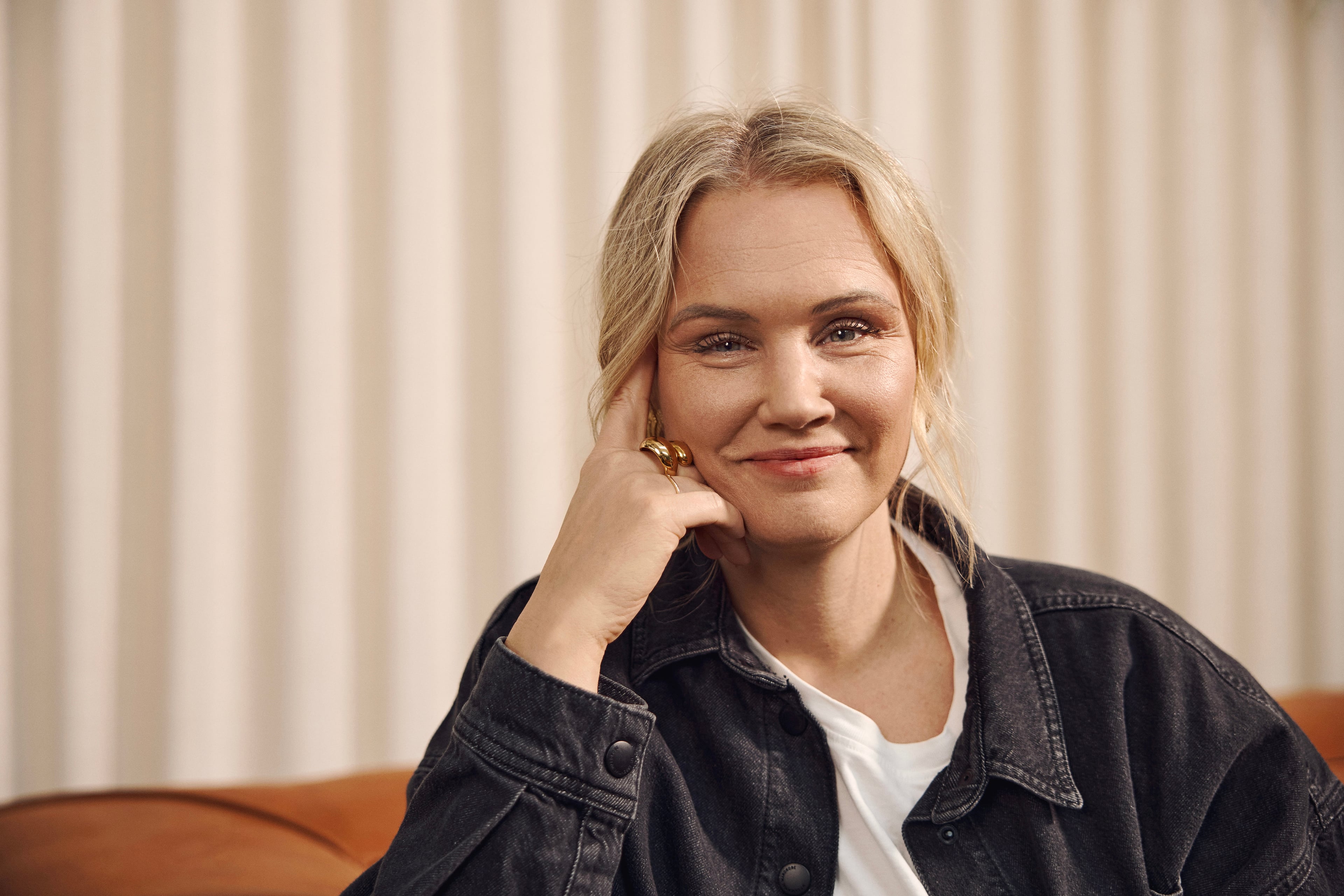 Woman with blonde hair in denim jacket smiling in front of light curtain