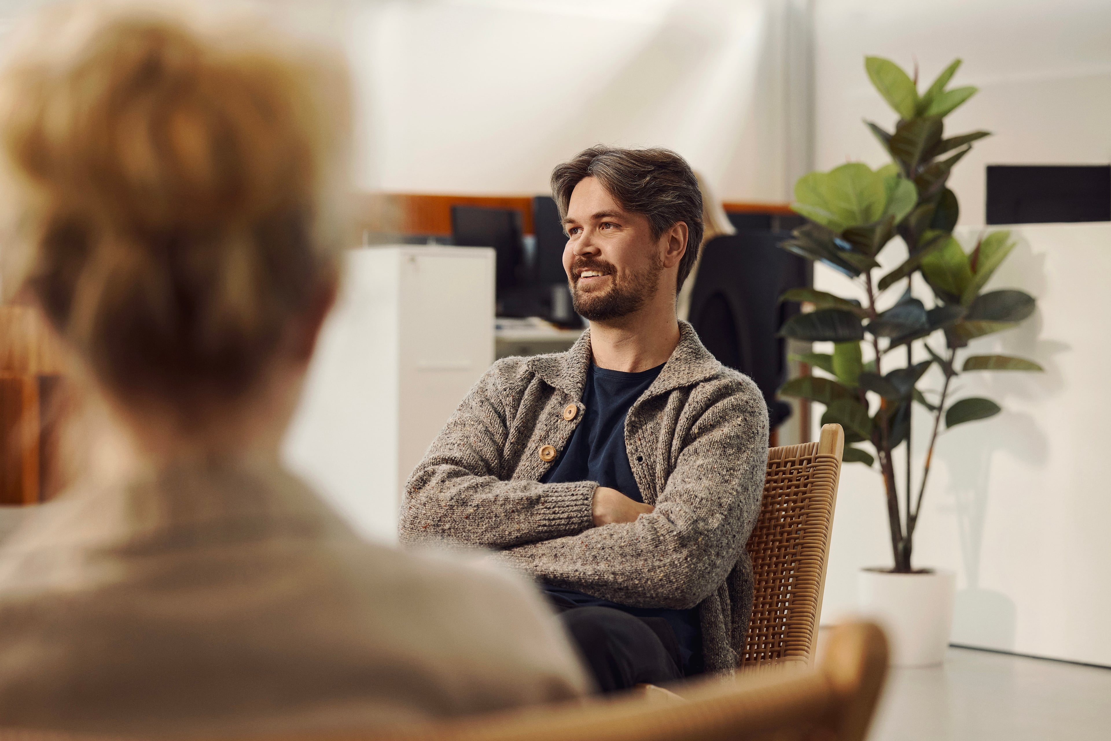 Man in conversation with woman in office with plant and furniture in background